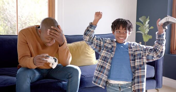 Happy african american father and son playing video games at home, slow motion