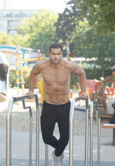 Fit man pulling up on bars while exercising on sports ground during intense workout outdoors.