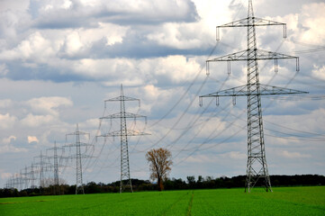 Hochspannungs-Freileitungen über Land: Energieübertragung des Stromnetzes zur Weiterleitung von elektrischer Energie vor bewölktem Himmel.