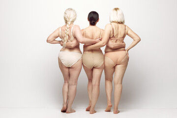 Back view of beautiful senior women in underwear standing against grey studio background. Natural...