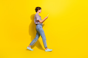 Fototapeta na wymiar Full size profile portrait of pretty girl use smart phone walk empty space ad isolated on yellow color background