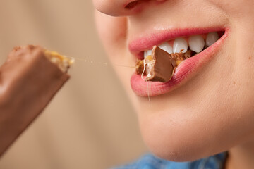 Close-up of a happy Caucasian woman's mouth biting off a piece of a creamy peanut butter bar. Front...