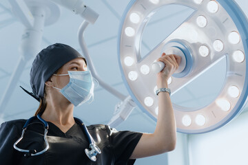 A nurse in a protective mask and suit stands next to the operating lamp. Preparation of the...