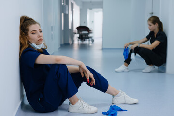 Two female doctors after surgery are sitting in the corridor of the clinic. Selective focus on a...