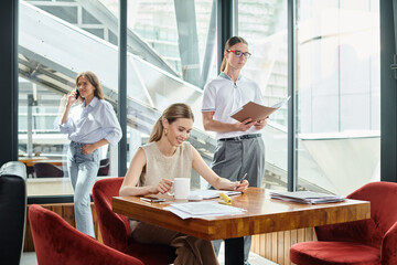two young colleagues in smart wear working on their papers and one talking on phone, coworking