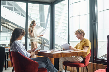 two young coworkers working with documents while their colleague talking on phone, coworking