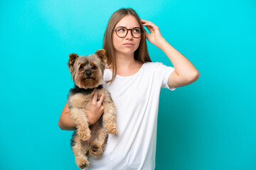 Young Lithuanian woman holding a dog isolated on blue background having doubts and with confuse...