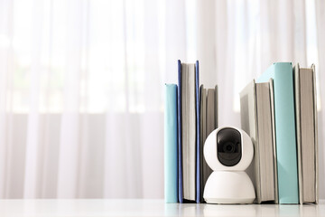 Home security camera and books on light background, space for text