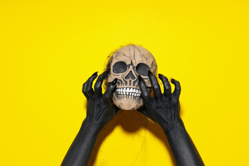 Skull in black female hands in web on yellow background