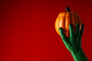 Pumpkin in green hand on red background, space for text
