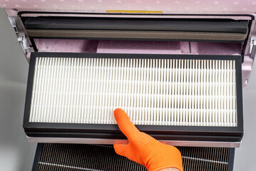 Replacing filters in a home ventilation system. A hand in an orange glove changes a Hepa filter.