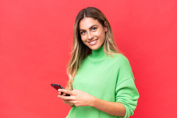 Young Uruguayan woman isolated on red background sending a message with the mobile