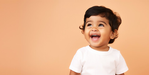 Adorable Indian toddler laughing wearing white shirt, isolated on pastel orange background