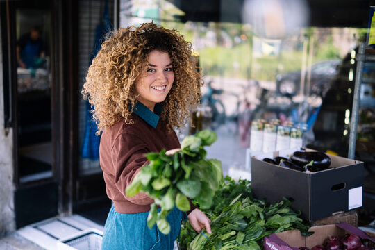 Smiling businesswoman holding leafy vegetables outside store