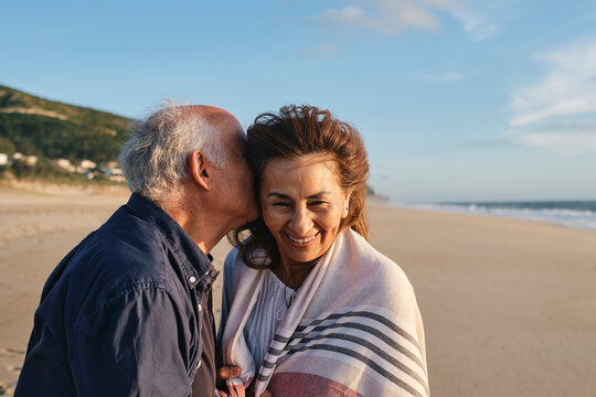 Senior man embracing happy woman at beach on sunny day