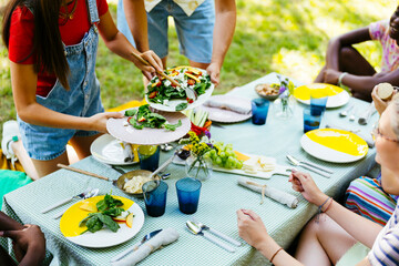 Friends serving food at picnic table in garden