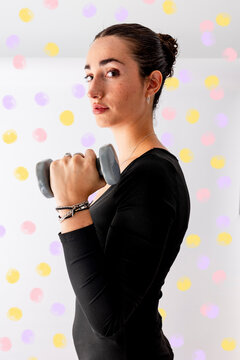 Beautiful woman exercising with dumbbell in front of patterned wall