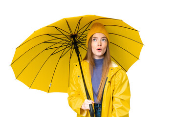 Young pretty woman with rainproof coat and umbrella over isolated chroma key background looking up...