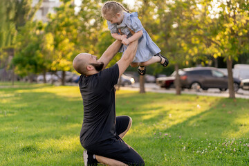 young father throwing his daughter in the air on a summer day in park, happy moments in life