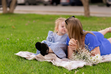 young happy mother and daughter having fun in the park laying on the ground on the grass