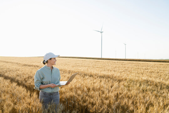 Smiling farmer with laptop at wheat field