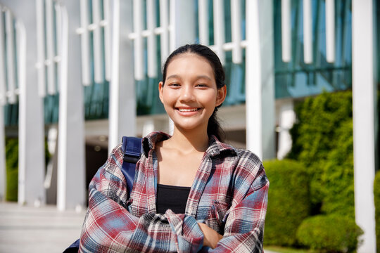 Happy student with arms crossed standing in front of university