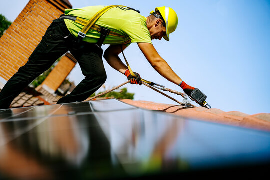 Engineer wearing hardhat using drill machine to install solar panel on roof