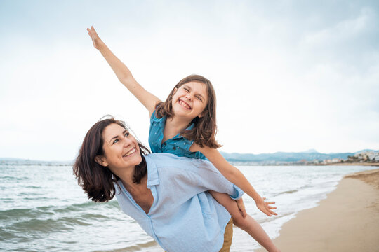Happy woman giving piggyback ride to daughter at beach