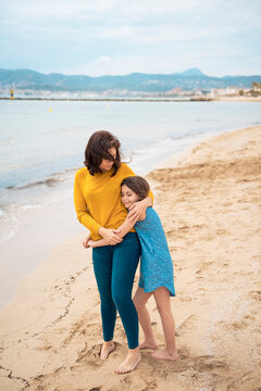 Smiling girl hugging mother in front of sea on coastline at beach