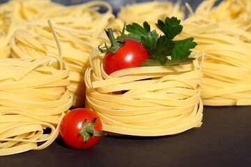 Several pieces of round pasta with red tomatoes lie on a black background.	