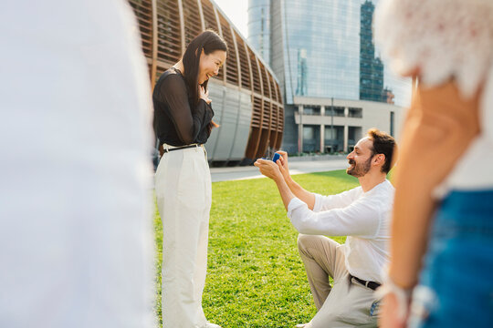 Smiling man proposing woman with ring at park