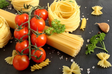 Several pieces of round pasta with red tomatoes lie on a black background.