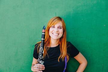 Happy redhead woman holding clarinet in front of green wall