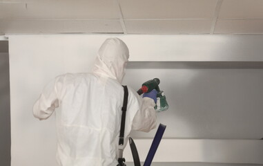 Worker paints wall white with spray gun. Painter in protective suit with spray gun concept