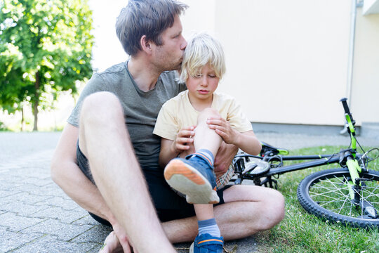 Father kissing and caring son fallen down from bicycle at footpath