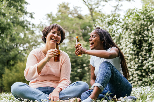 Happy friends enjoying beer sitting together at park