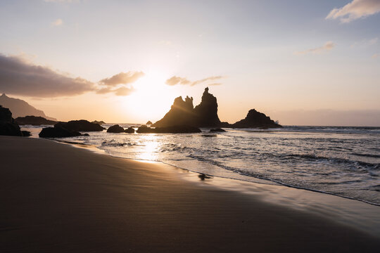 Silhouette of waves and rocks on beach at sunset
