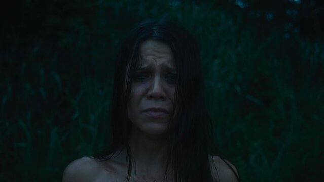 A tired, frightened girl with abrasions in a bloody dress cries looking at the camera