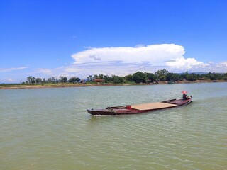  a landscape image of a boat on the water. The boat is in a lake or river, with a clear sky and clouds in the background. It is a peaceful scene of outdoor boating