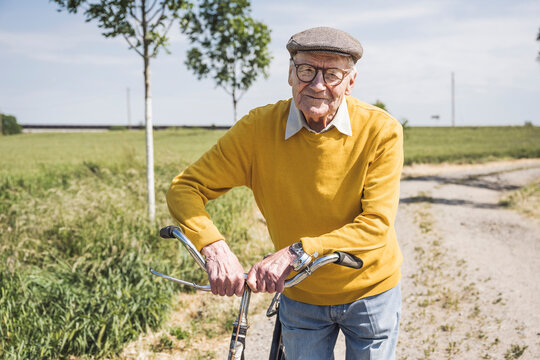 Smiling senior man standing with bicycle on sunny day