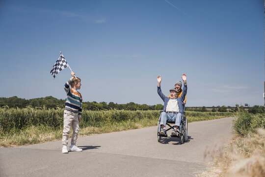Boy holding checkered flag with senior man sitting in wheelchair on road