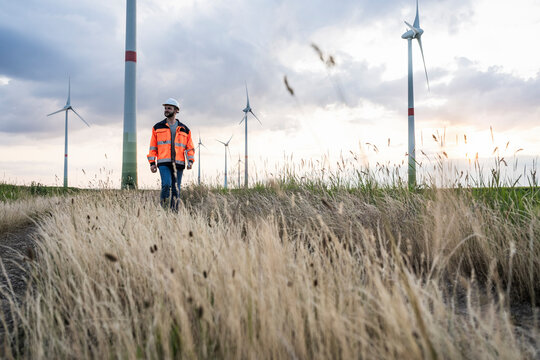 Engineer walking in grass with wind turbines in background