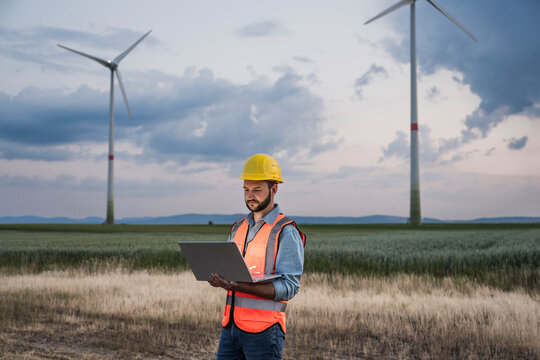 Engineer in reflective clothing using laptop with wind turbines in background