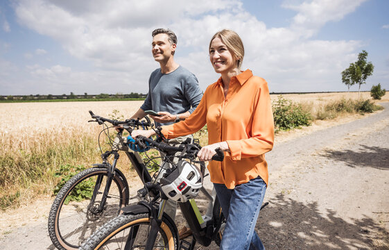 Man holding smart phone by woman wheeling bicycle on road