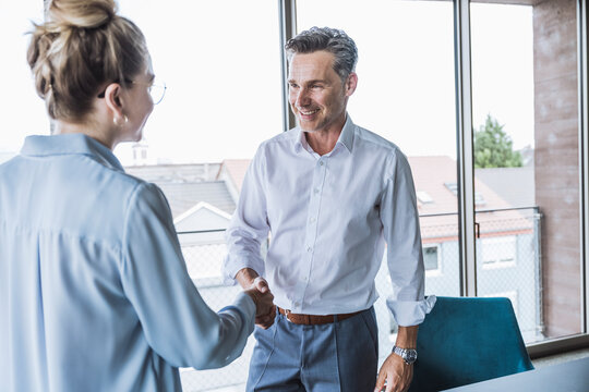 Smiling businessman shaking hands with businesswoman in office