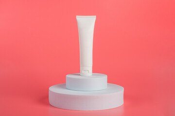 Plastic white tube for cream or lotion. Skin care or sunscreen cosmetic with stylish props on pink background 