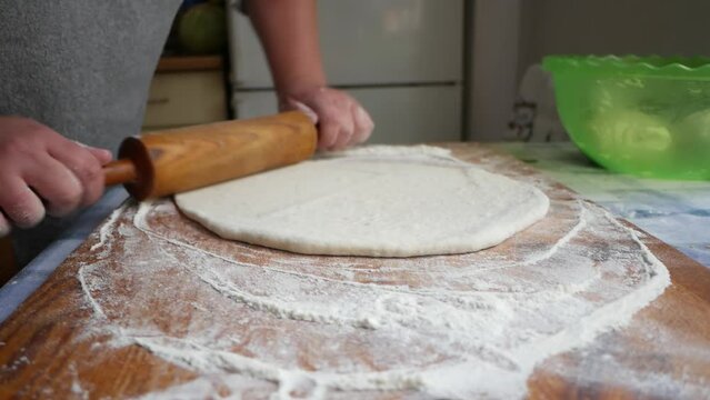 A young housewife kneads yeast dough on a wooden board. 