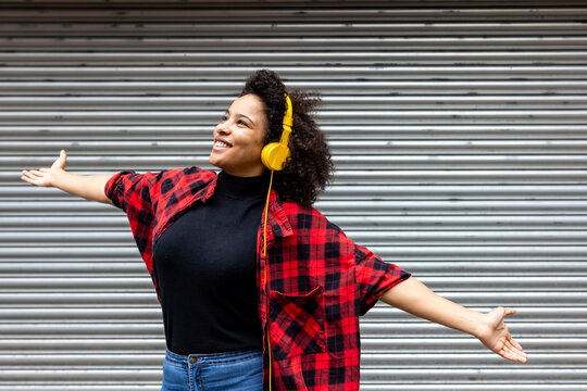 Smiling woman wearing headphones standing with arms outstretched in front of shutter