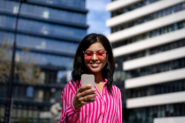 Happy woman using smart phone in front of buildings