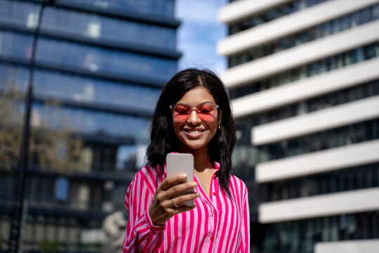 Happy woman using smart phone in front of buildings